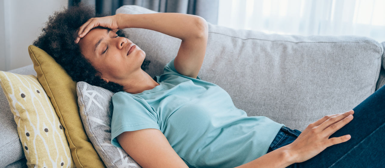 Sick young woman lying on the couch and holding her head with hand. Ill woman lying on the sofa with high temperature.